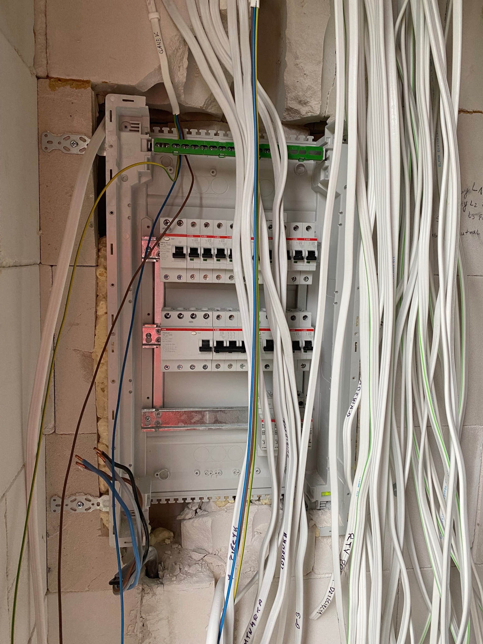 Rozdzielnica elektryczna w trakcie montażu w surowym wnętrzu. Widoczne liczne przewody, zabezpieczenia i elementy montażowe. Praca w toku, instalacja elektryczna.