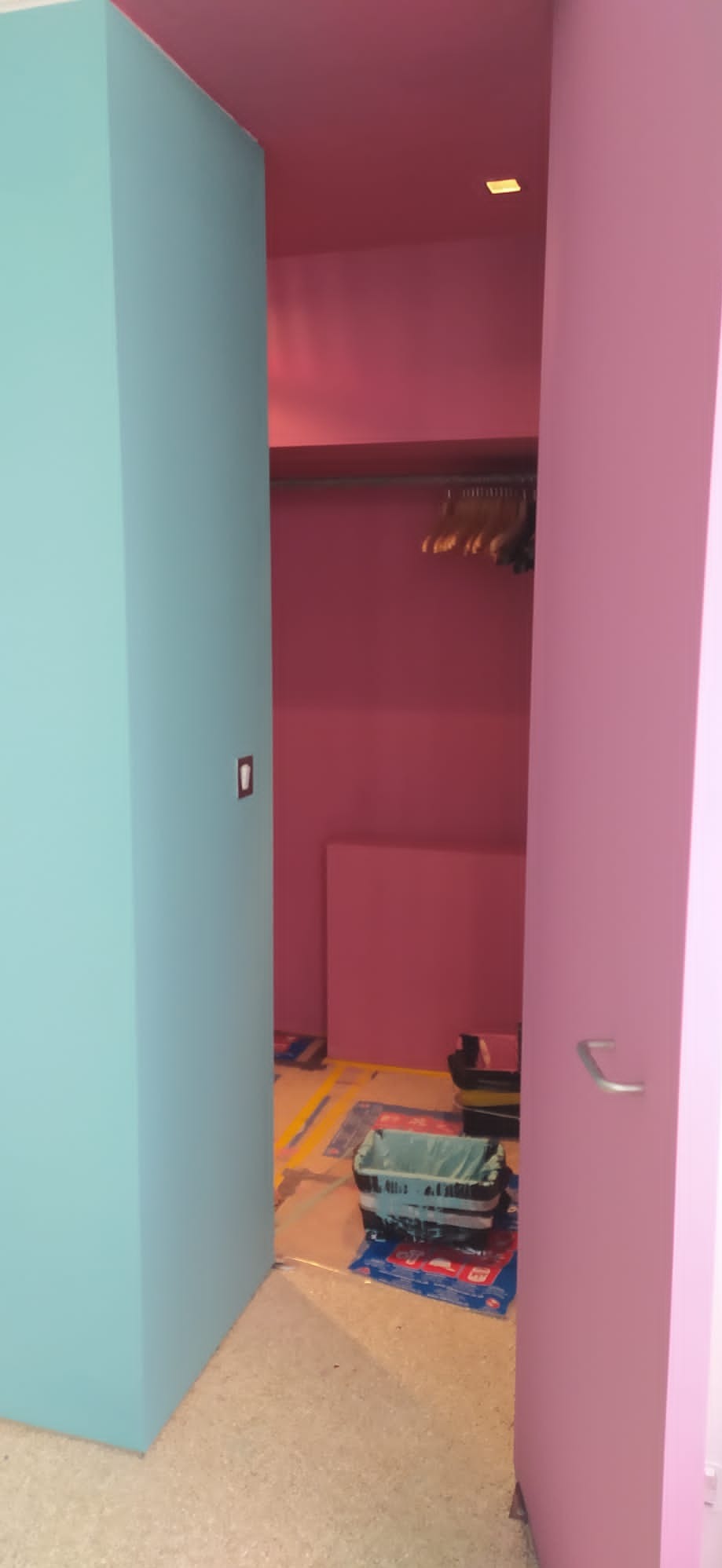 Malowanie ścian na różowo i niebiesko w garderobie, widoczne zabezpieczenia podłogi i akcesoria malarskie.