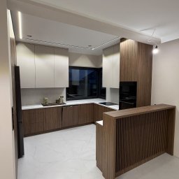 Mateusz Mróz - Nowoczesna kuchnia z drewnianymi i białymi szafkami, marmurowym blatem i oświetleniem LED. Widoczny fragment wyspy kuchennej z dekoracyjnymi listwami.