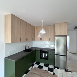 Mateusz Mróz - Nowoczesna kuchnia z zielonymi szafkami dolnymi i drewnopodobnymi górnymi, czarno-biała podłoga, srebrna lodówka. Lampa w folii ochronnej.