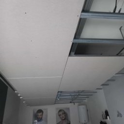 AleksanderBorsukUsługiRemontowe - Montaż sufitu podwieszanego z płyt kartonowo-gipsowych na metalowej konstrukcji w pomieszczeniu z elementami wyposażenia salonu fryzjerskiego w tle.