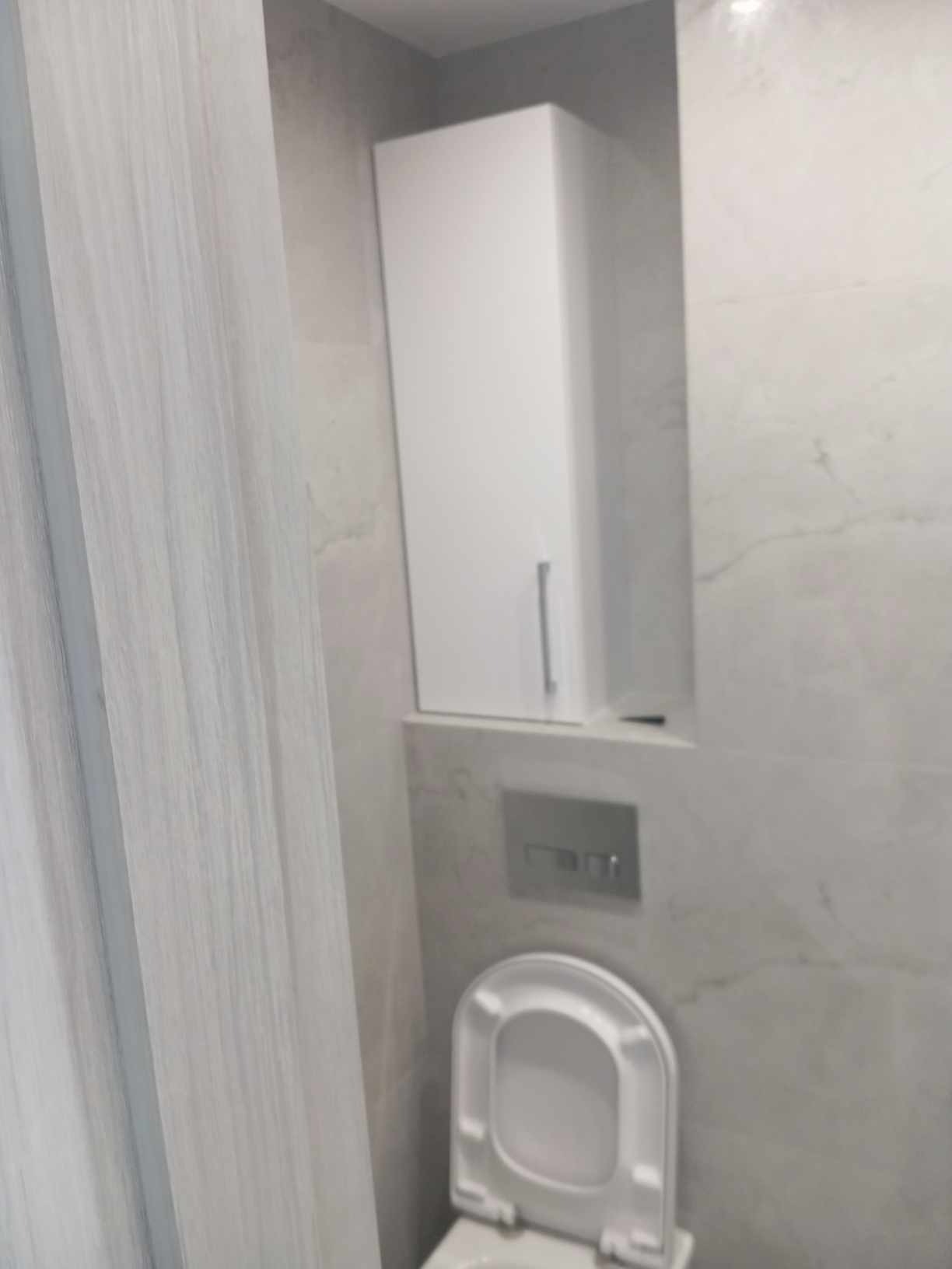 Nowoczesna łazienka z wiszącą białą szafką, marmurowymi płytkami na ścianach i otwartą toaletą.