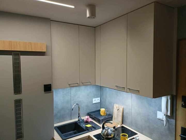 Wykończona kuchnia w Bochni: szare szafki wiszące z podświetleniem LED nad blatem z czarnym zlewem i płytą indukcyjną, widoczny fragment lodówki.