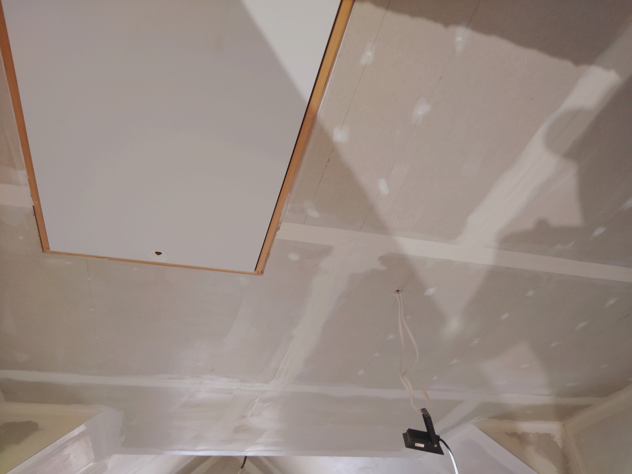 Sufit poddasza po szpachlowaniu, widoczne łączenia płyt gipsowych i otwór rewizyjny. Kabel zwisa z sufitu. Ujęcie z dołu, perspektywa zbieżna.