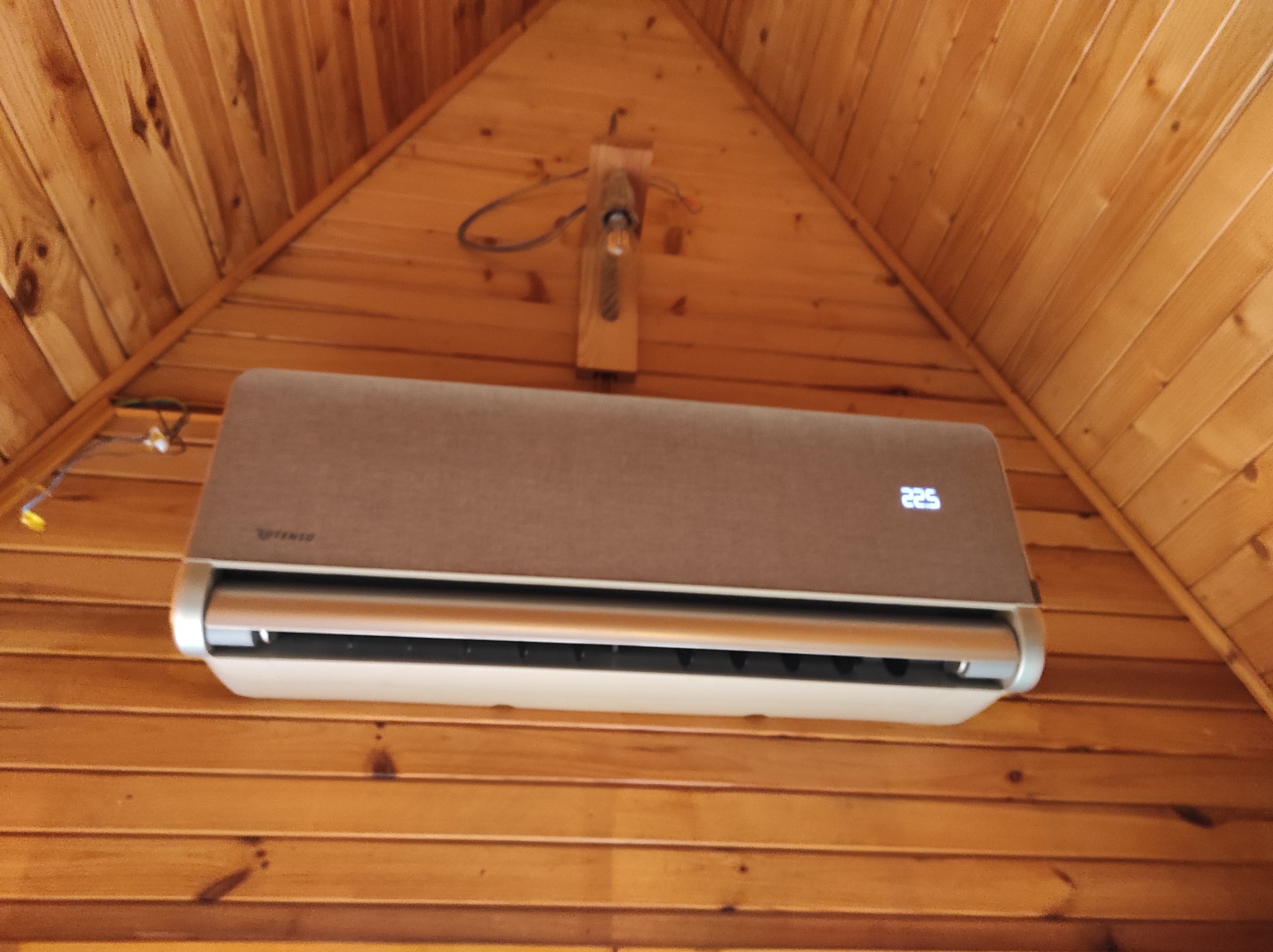 Klimatyzator Rotenso Caramel zamontowany na drewnianej ścianie w pomieszczeniu o drewnianym wykończeniu, widoczny wyświetlacz z temperaturą 22.5 stopnia.