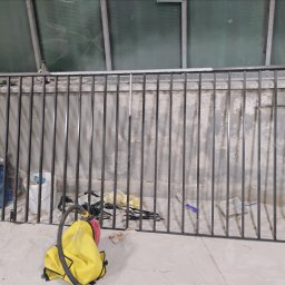 Pablopiask .Piaskowanie - Metalowa barierka po obróbce, widoczny sprzęt do czyszczenia i pozostałości po procesie na podłodze.