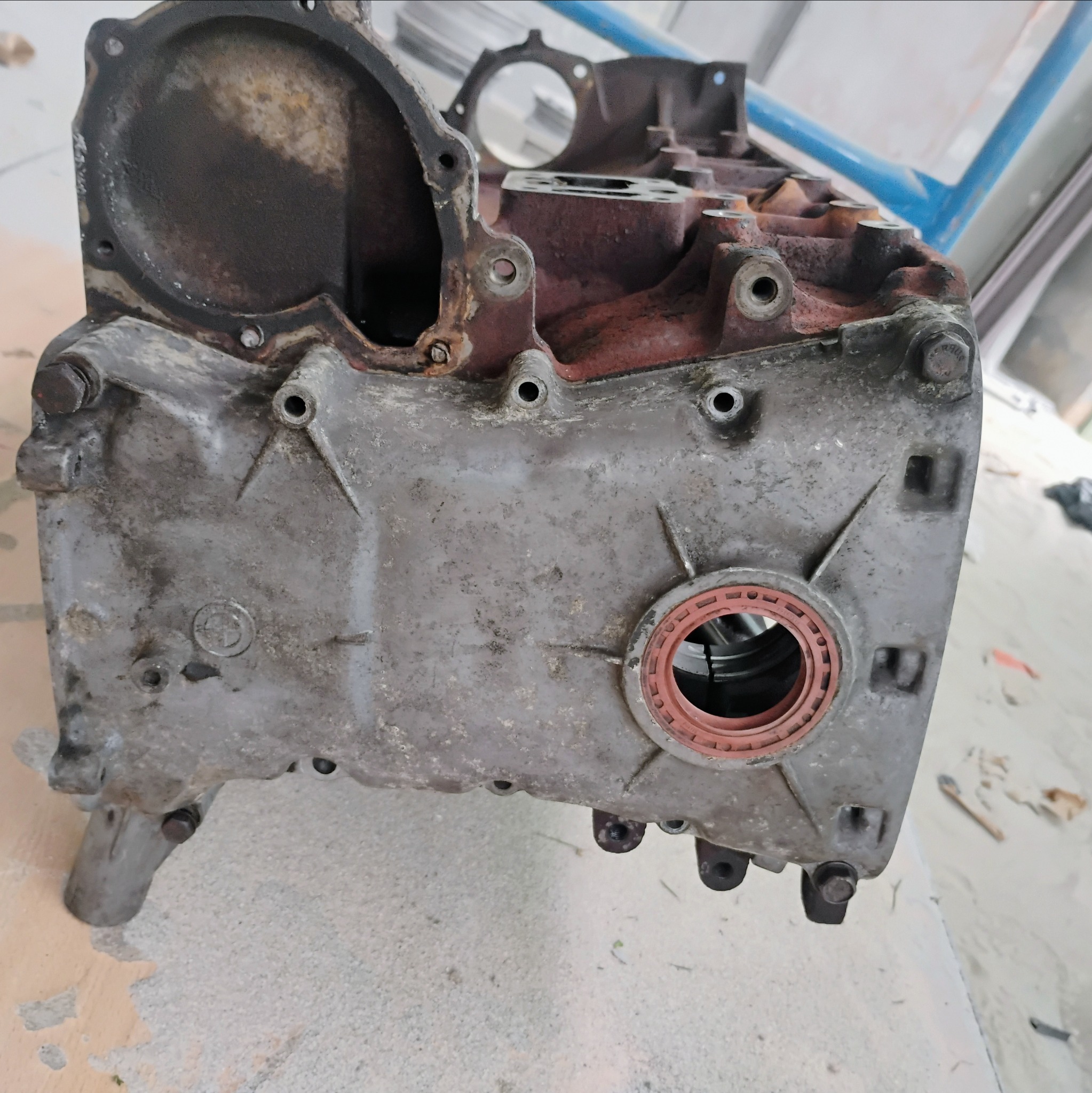 Brudny, zdemontowany blok silnika samochodowego z widocznymi śladami rdzy i oleju, ukazujący otwory montażowe i uszczelkę.