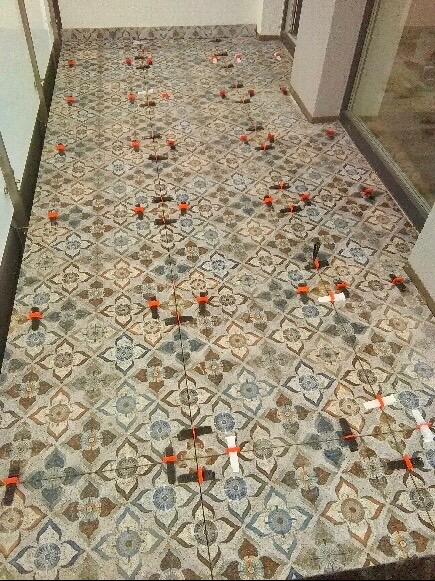 Układanie wzorzystych płytek podłogowych z systemem poziomowania, widoczne pomarańczowe kliny i białe paski dystansowe.