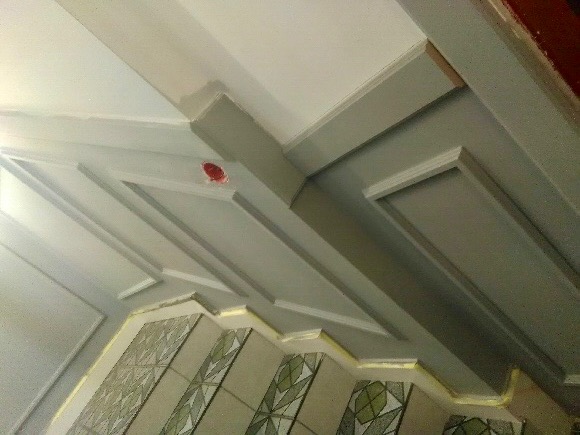 Sufit z dekoracyjnymi listwami i panelami, pomalowany w odcieniach szarości i bieli, widoczny fragment ściany z mozaiką.
