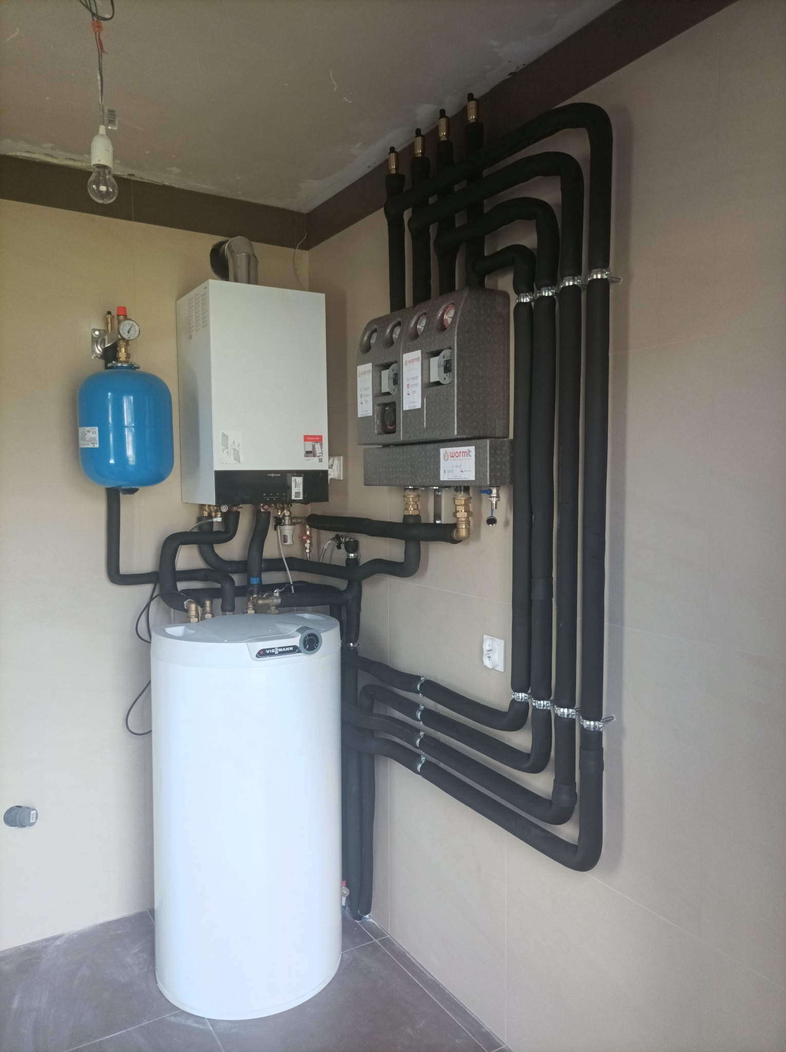 Zmontowany piec gazowy Viessmann z zasobnikiem i czarnymi rurami w izolacji, zainstalowany w pomieszczeniu z beżowymi ścianami i podłogą wyłożoną płytkami.