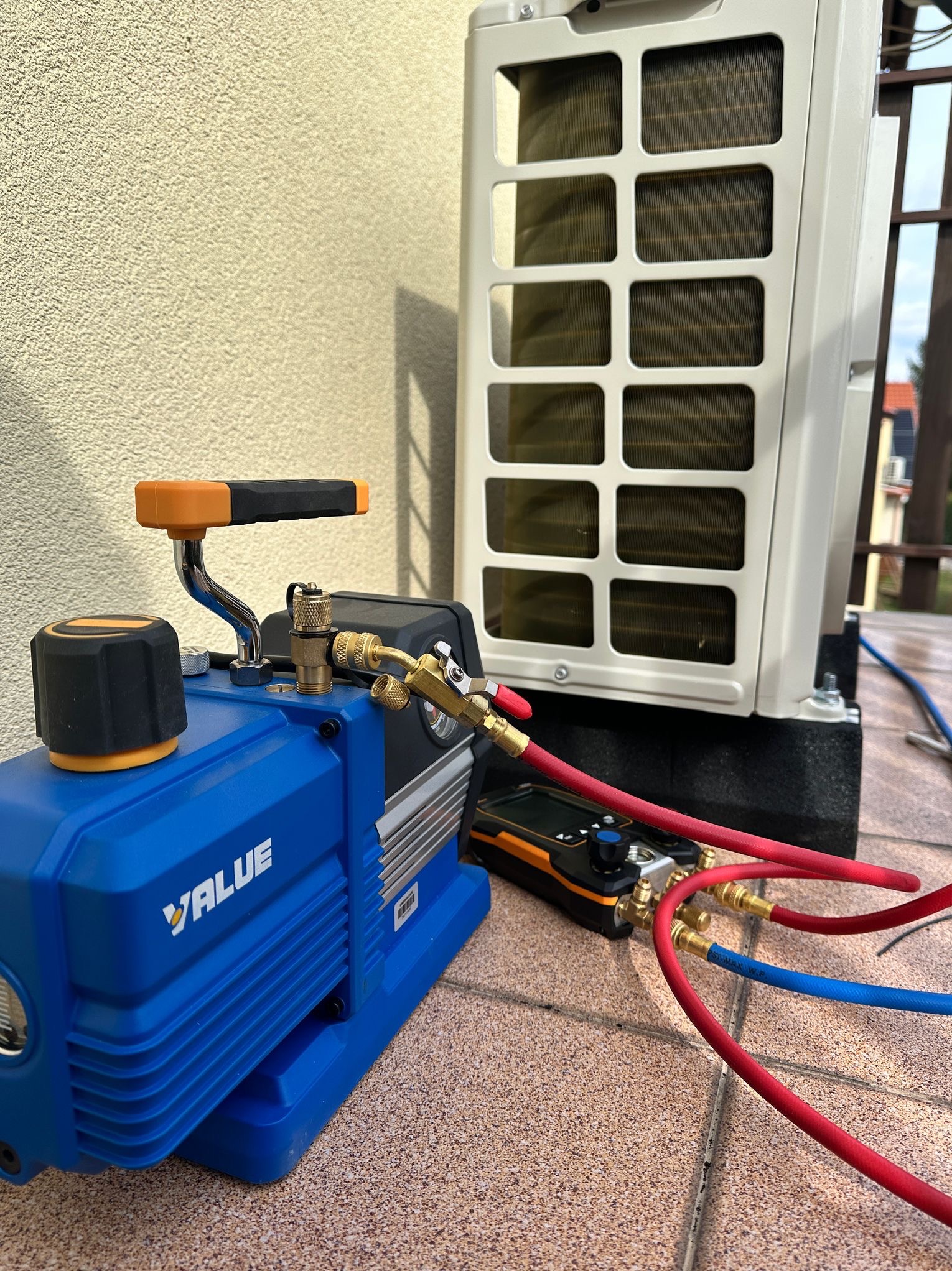 Podłączenie pompy próżniowej VALUE do zewnętrznej jednostki klimatyzacji na balkonie, widoczne manometry i przewody chłodnicze.