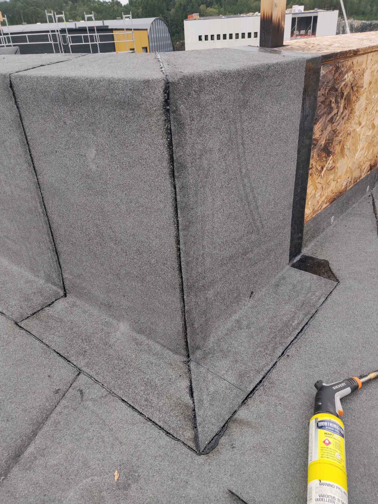 Szczegółowe wykończenie narożnika dachu pokrytego papą termozgrzewalną, z widocznym palnikiem dekarskim. Precyzyjne łączenia i estetyczne wykonanie.