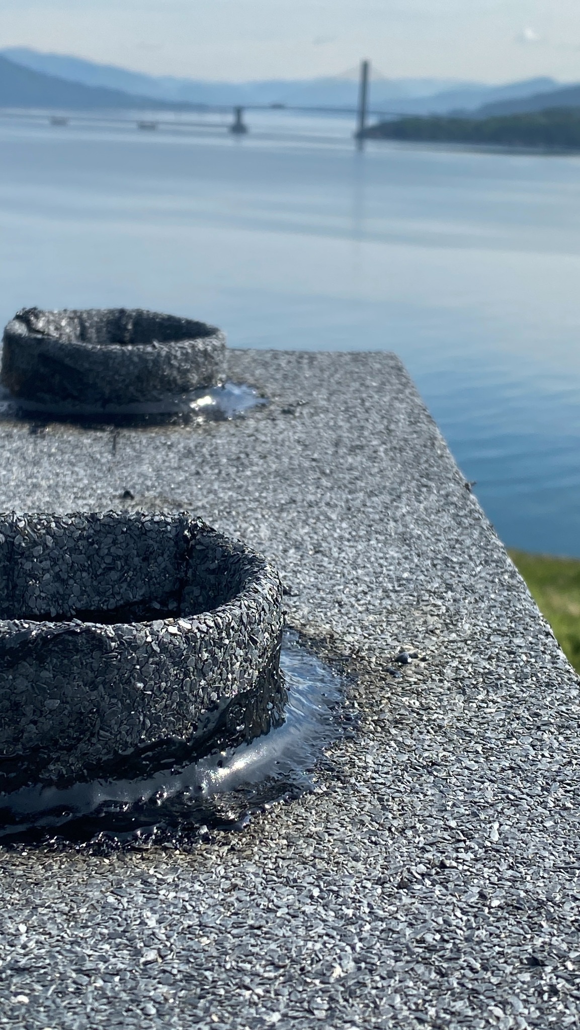 Wykończony dach pokryty papą z kominkami wentylacyjnymi na tle krajobrazu z wodą i górami w oddali, wykonany z bliska, prezentujący detale pokrycia.