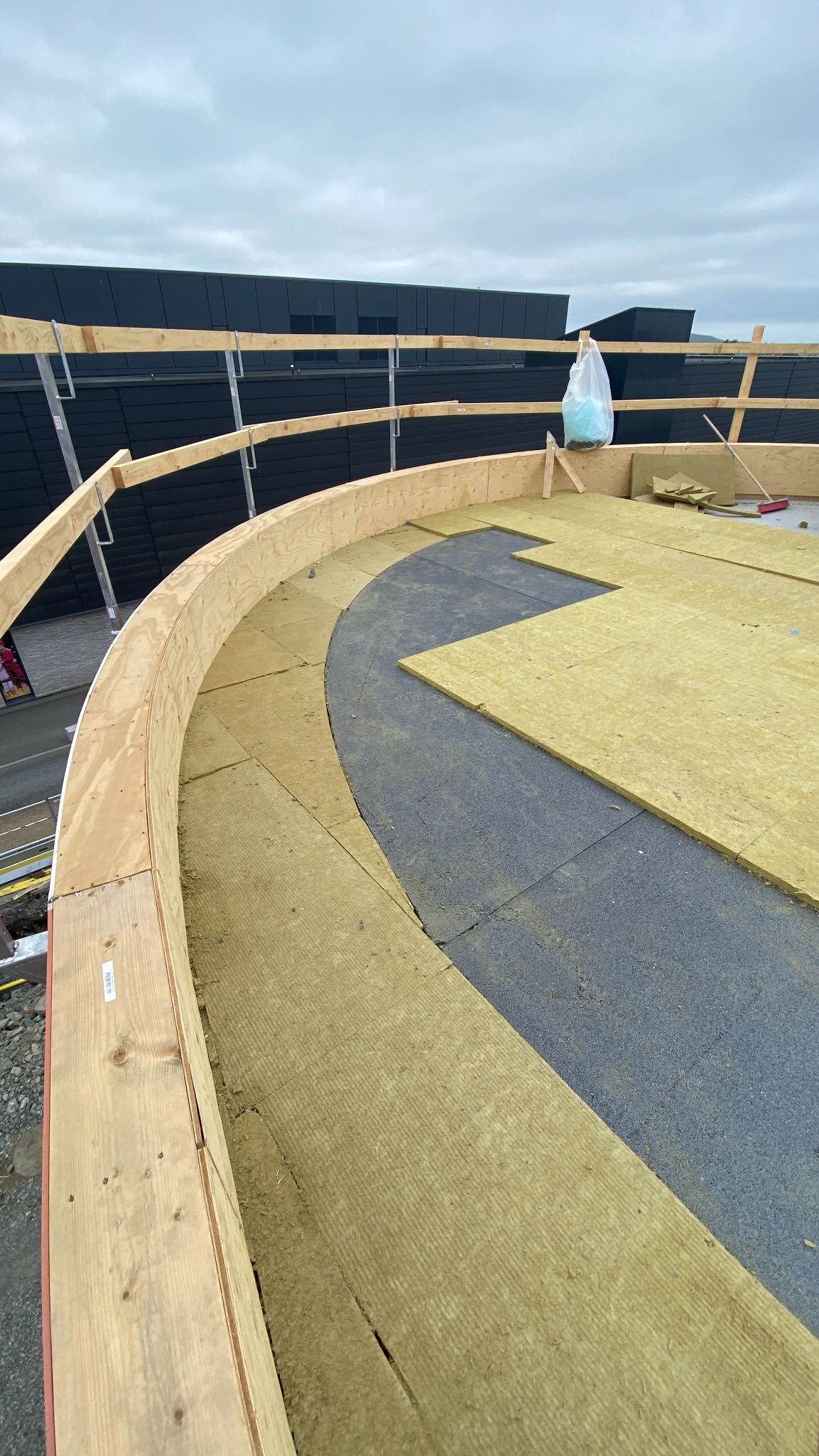 Izolacja dachu płaskiego z drewnianą konstrukcją krawędziową i częściowo ułożonymi płytami izolacyjnymi. Widok z góry na budowę dachu.