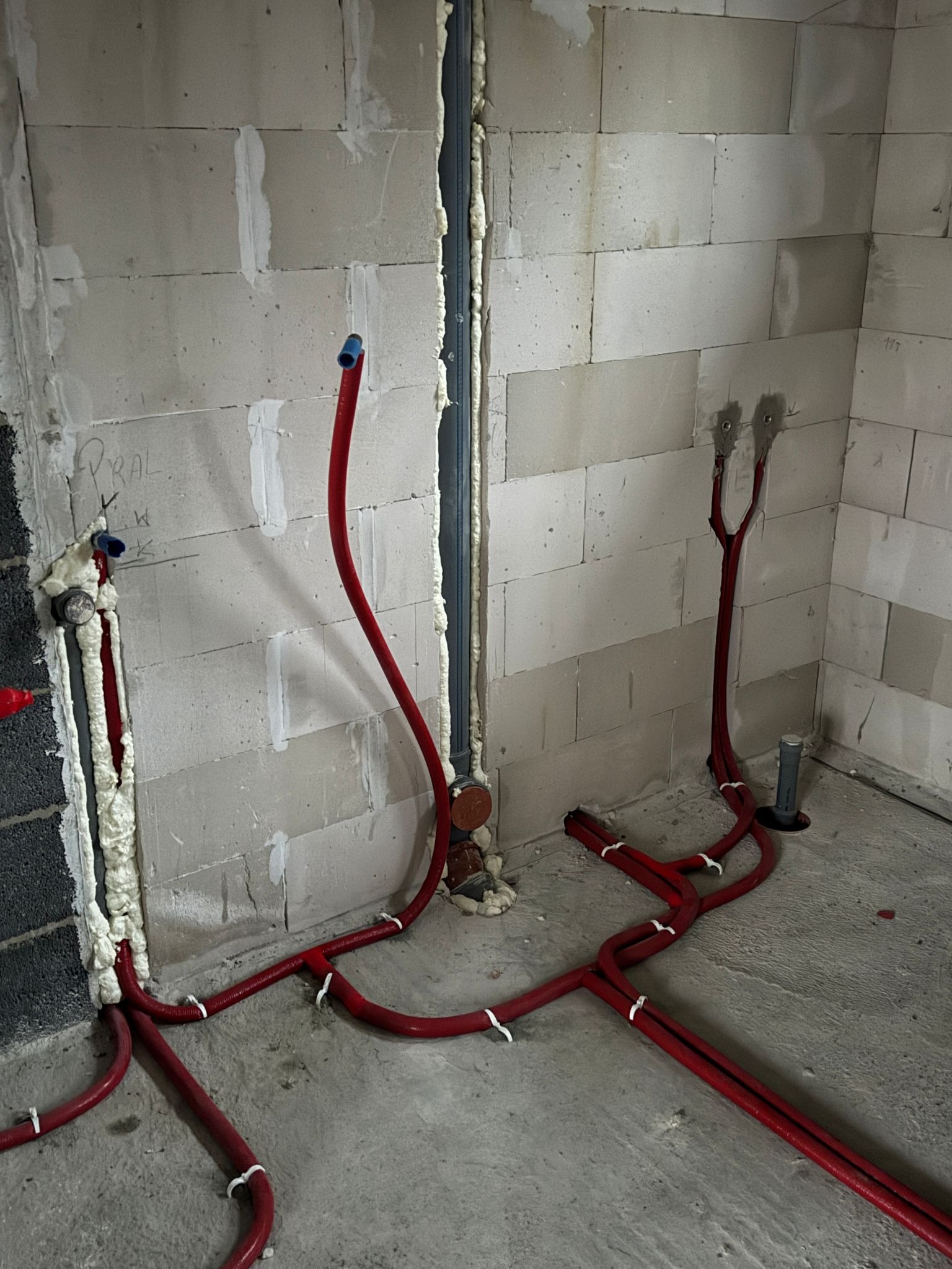 Czerwone rury instalacji wodnej w trakcie montażu w surowym wnętrzu budynku w Kielanówce, zabezpieczone pianką montażową w miejscach przejść przez ściany z betonu komórkowego.