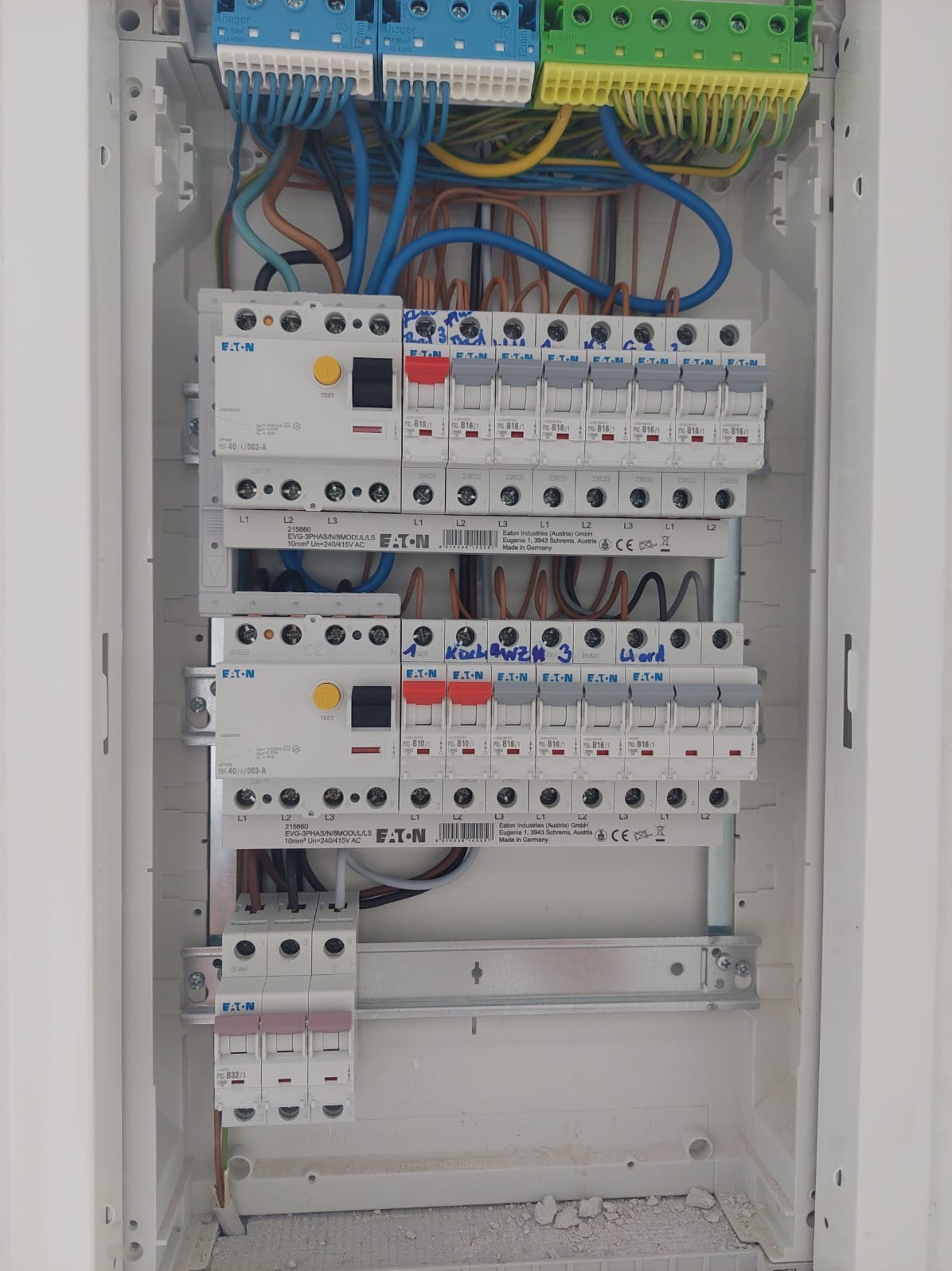 Szczegółowe ujęcie tablicy rozdzielczej z zainstalowanymi bezpiecznikami i okablowaniem, widoczne oznaczenia producenta Eaton oraz ręczne notatki na obudowie, całość w białej obudowie z widocznymi...