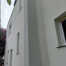 Andrii Matiitsiv - Jasna, świeżo otynkowana elewacja dwukondygnacyjnego budynku z wąskimi oknami i wyraźną fakturą tynku, uchwycona pod kątem z dołu.