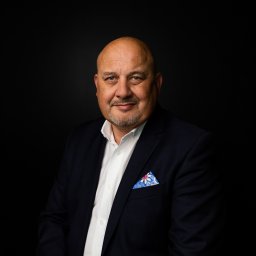 Fotographiki Adam Głodkowski - Portret uśmiechniętego mężczyzny w granatowej marynarce i białej koszuli z wzorzystą poszetką na czarnym tle.