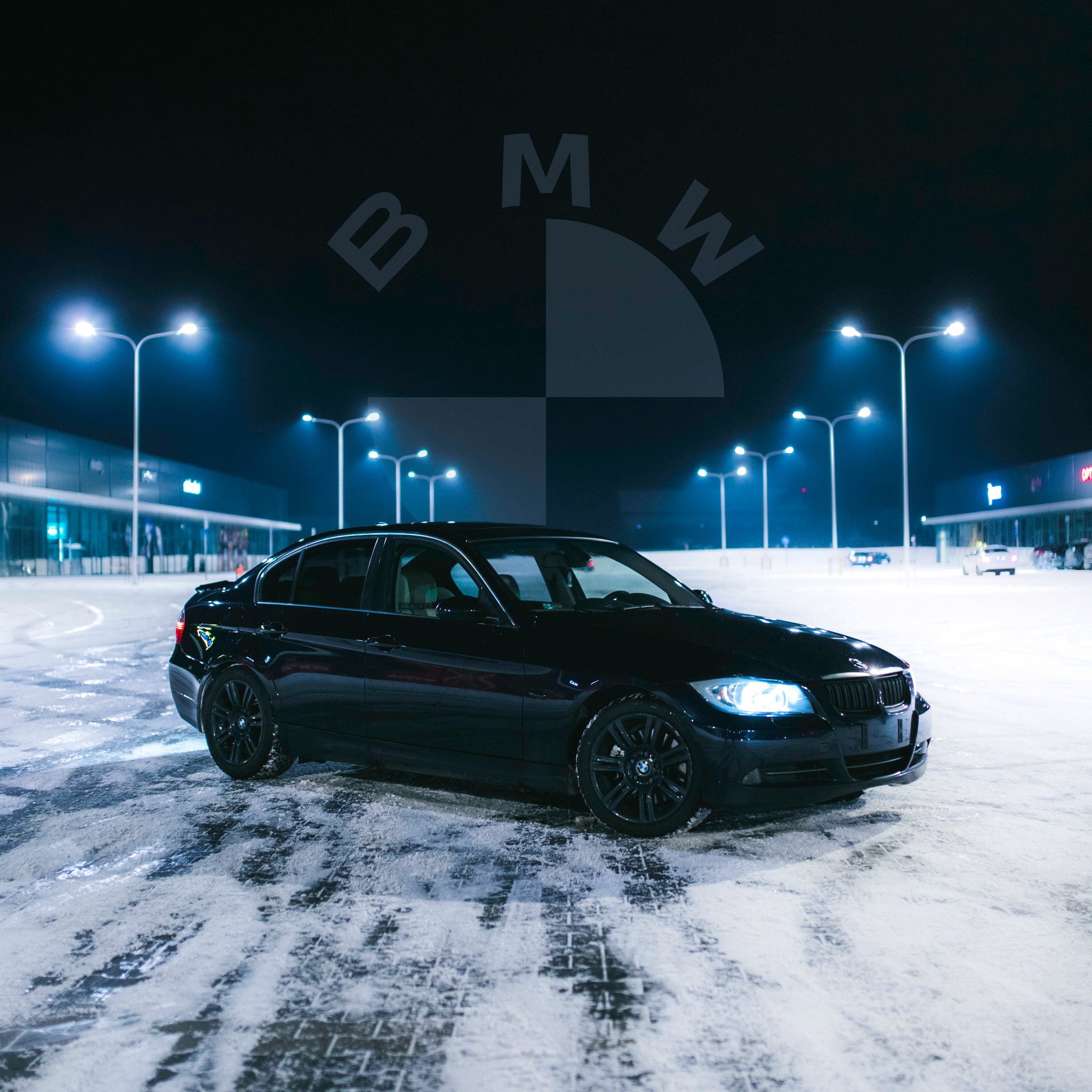 Czarny samochód marki BMW na ośnieżonym parkingu nocą, z widocznym znakiem marki w tle.
