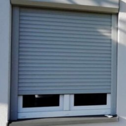 BramAD Adrian Kulik - Zasłonięte okno szarą roletą zewnętrzną, widok z bliska na elewację budynku.