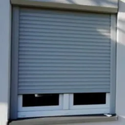 Zasłonięte okno szarą roletą zewnętrzną, widok z bliska na elewację budynku.