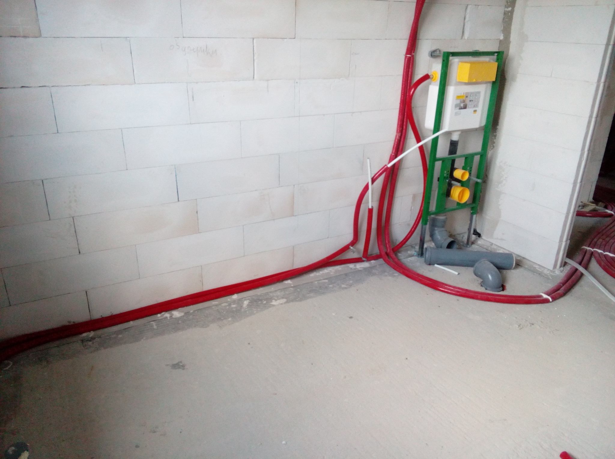 Surowy stan instalacji hydraulicznej w Świdnicy: czerwone rury prowadzone wzdłuż ściany z betonu komórkowego, widoczny stelaż podtynkowy WC z żółtymi elementami oraz fragment instalacji...