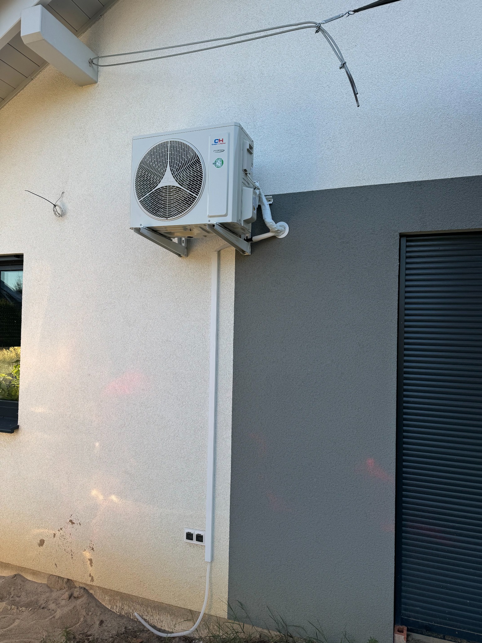 Zamontowana jednostka zewnętrzna klimatyzacji na elewacji budynku w Komorowie, z widocznymi przewodami i osłonami instalacyjnymi.