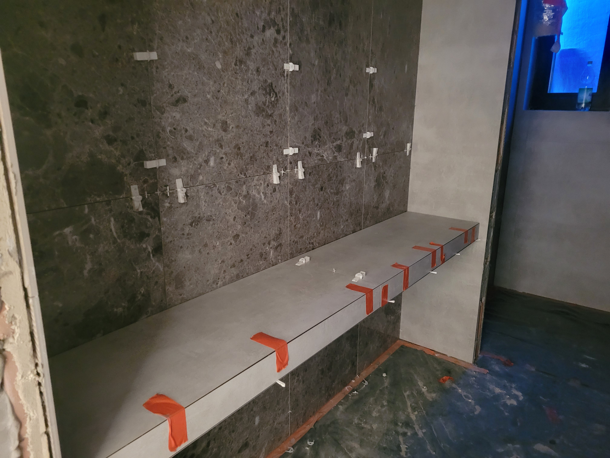 Montaż płytek imitujących marmur na ścianie i blacie w łazience, z użyciem krzyżyków dystansowych i taśmy maskującej.