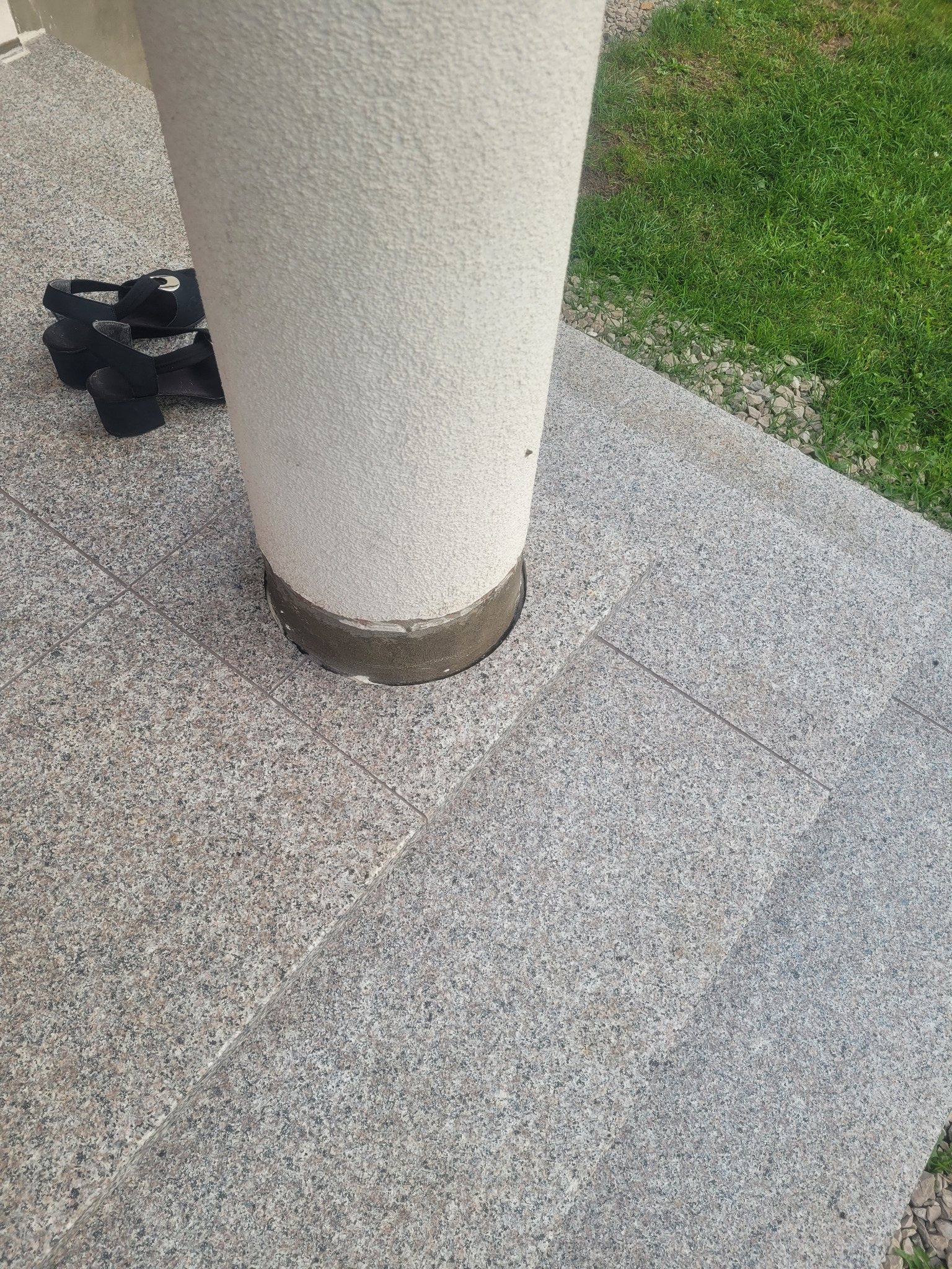 Wykończone granitowe schody z kolumną, z pozostawionymi obok butami na obcasie.