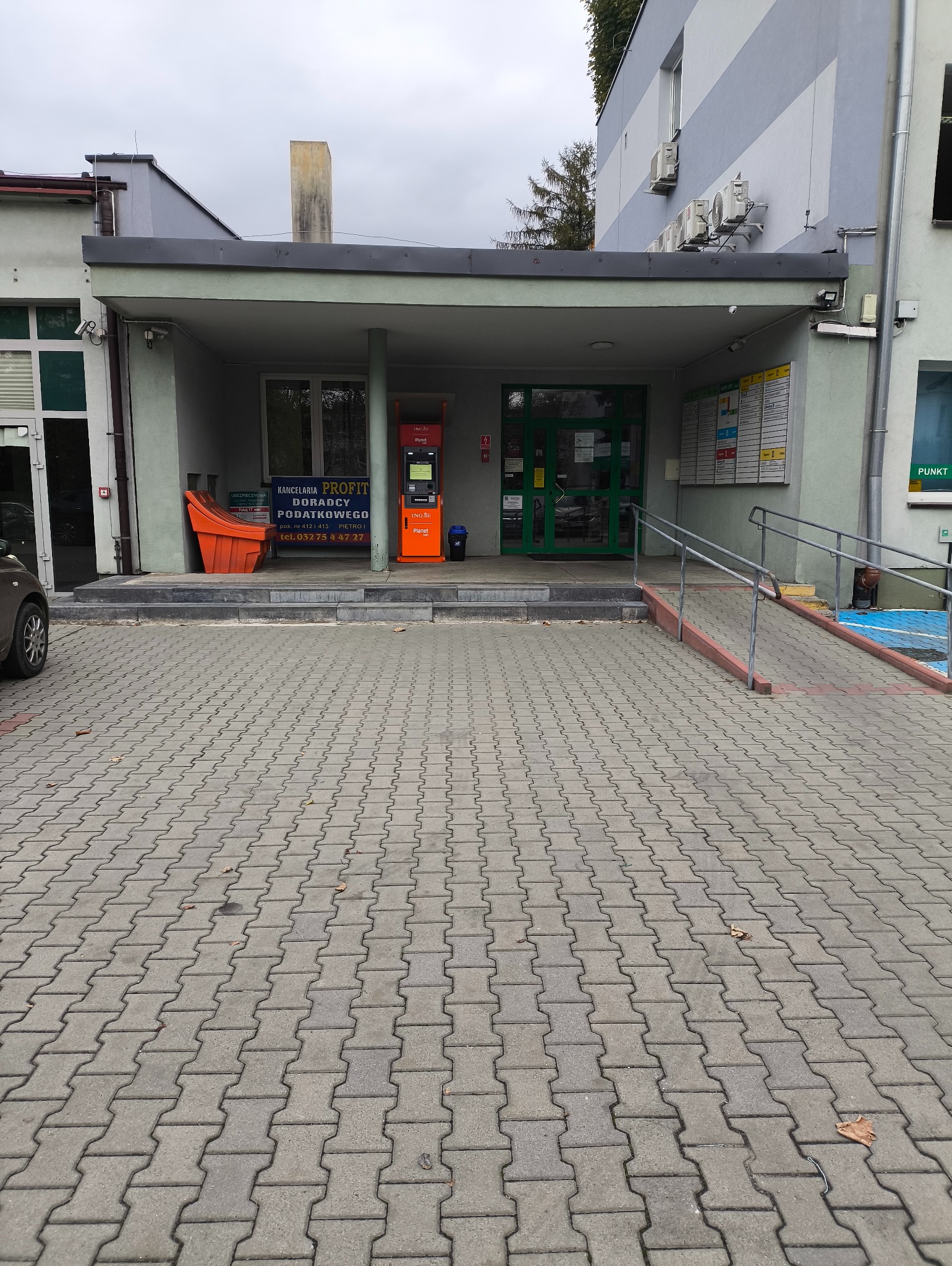 Wejście do biura Kancelarii Profit Doradcy Podatkowego z pomarańczowym bankomatem ING Planet po prawej stronie i rampą dla wózków inwalidzkich.