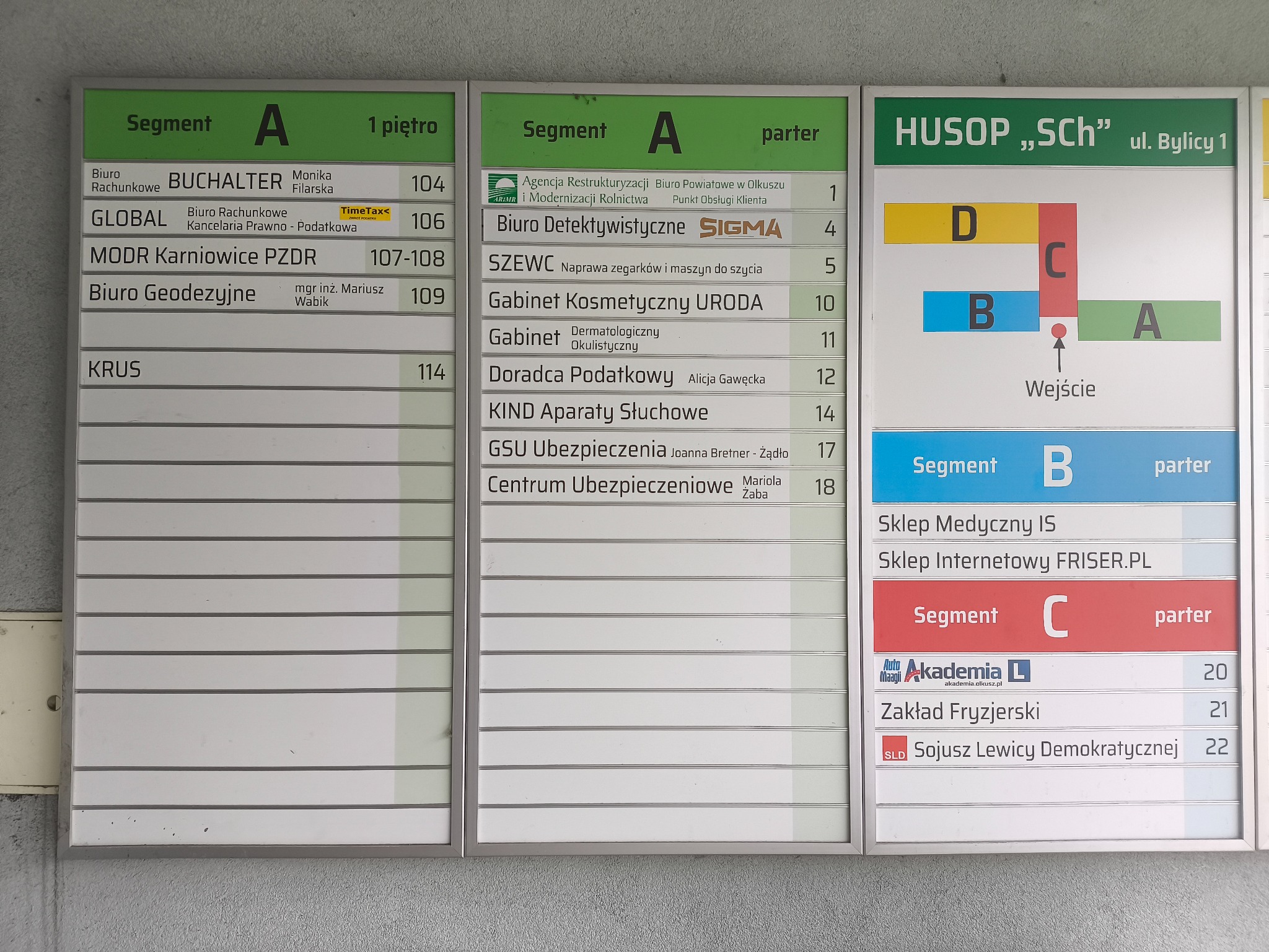 Tablica informacyjna w budynku z listą firm i instytucji, w tym Biuro Detektywistyczne SIGMA na parterze, segment A, numer 4.