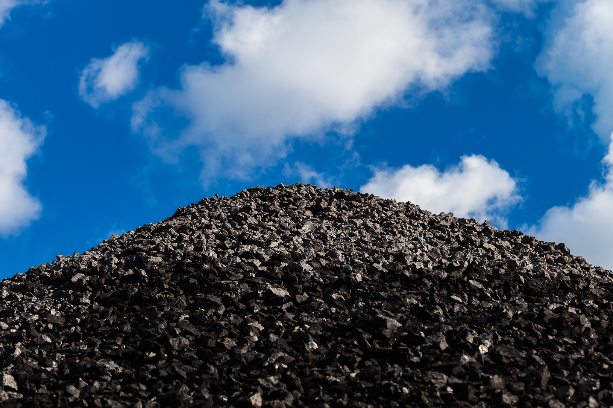 Góra czarnego, błyszczącego węgla na tle błękitnego nieba z białymi obłokami.