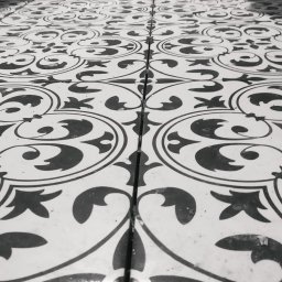 KM.BuD - Czarno-biała podłoga wyłożona wzorzystymi płytkami ceramicznymi, widoczne przewody i fragment toalety w tle.