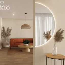 Nowoczesne wnętrze z okrągłym lustrem z podświetleniem LED, odbijającym część salonu z pomarańczową sofą i drewnianym stolikiem kawowym.