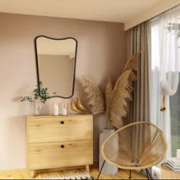 Komoda z dwoma szufladami, na niej lustro w czarnej ramie, świece, szklany wazon z zielonymi gałązkami i drewniane figurki ptaków, obok krzesło z plecionki na metalowych nogach i wazon z suchymi...