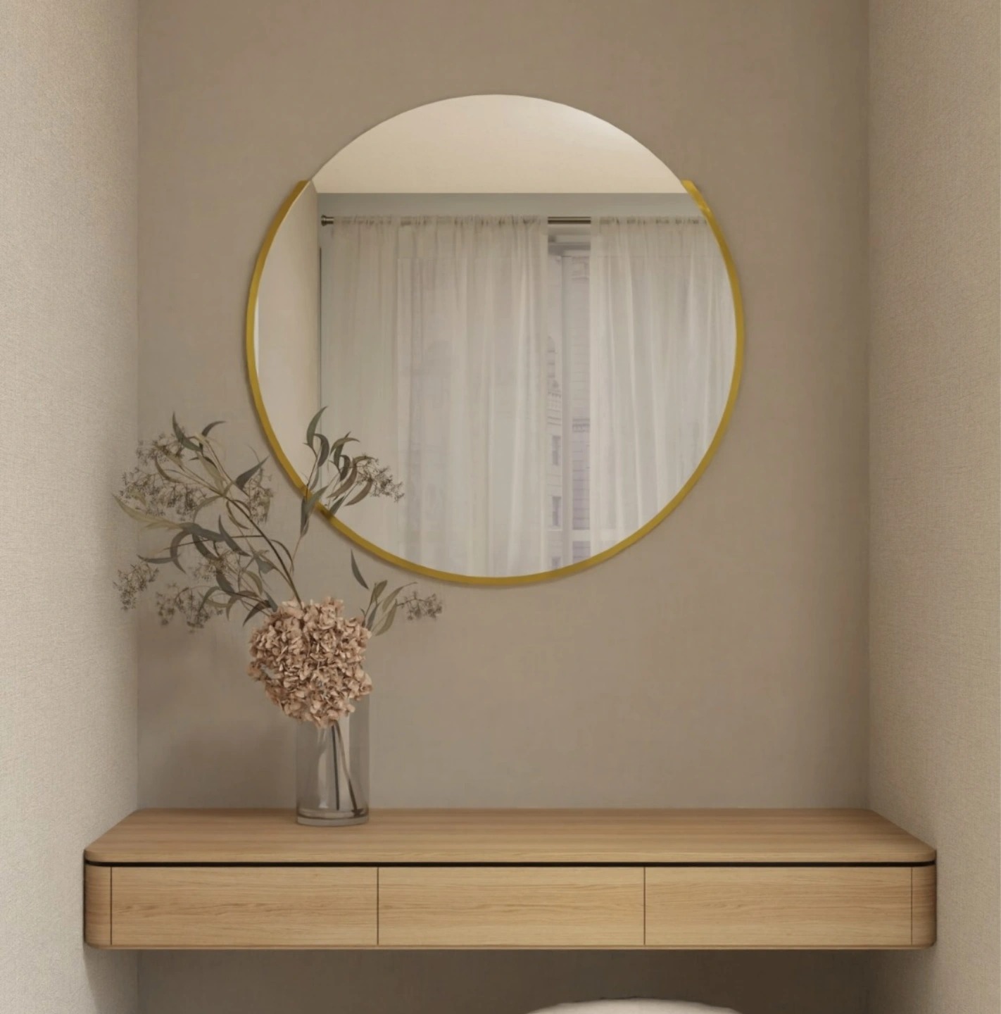 Okrągłe lustro w złotej ramie zawieszone nad drewnianą konsolą z trzema szufladami, uzupełnione wazonem z suszonymi kwiatami, na tle beżowej ściany i białych zasłon w oknie.