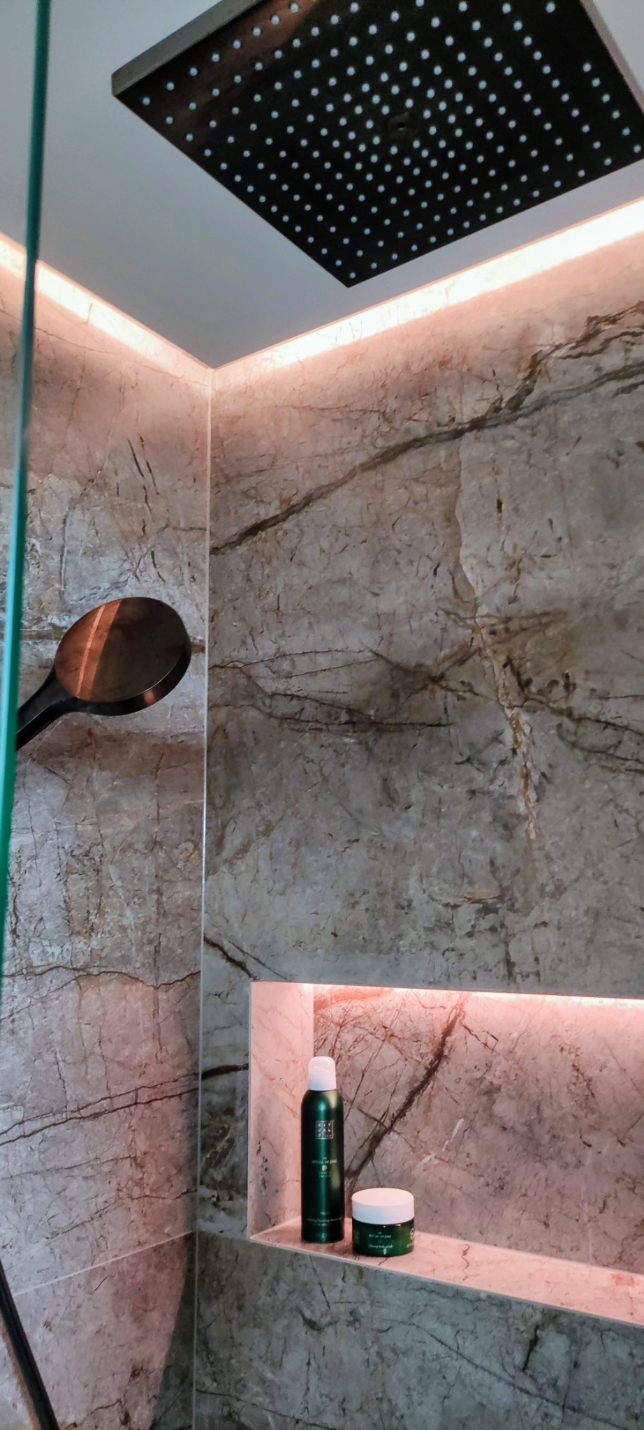 Nowoczesna kabina prysznicowa z marmurowymi ścianami, deszczownicą, wnęką z podświetleniem LED i kosmetykami Rituals.