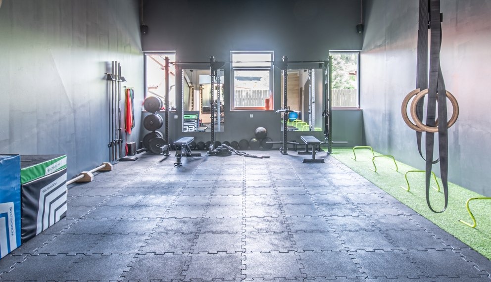 Sala treningowa Move Center: widok na sprzęt do ćwiczeń siłowych, podciągania i gimnastyki, w tym sztangi, obciążenia, skrzynie plyometryczne, drabinki i kółka gimnastyczne zawieszone na ścianie.