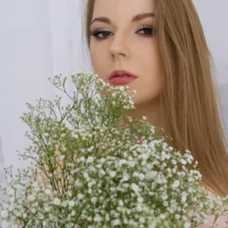 Portret kobiety z długimi, prostymi włosami, trzymającej bukiet białych gips&oacute;wek na jasnym tle.