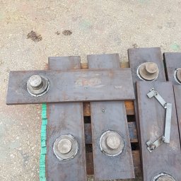 SKEMWELD PRZEDSIĘBIORSTWO WIELOBRANŻOWE PIOTR KUSZYŃSKI - Metalowe płyty z przyspawanymi elementami, ułożone na drewnianej palecie pomalowanej na zielono; widoczne spoiny i ślady obróbki.