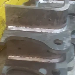 Stos metalowych elementów konstrukcyjnych połączonych spoiną, widoczne ślady obróbki i niedoskonałości spoin.