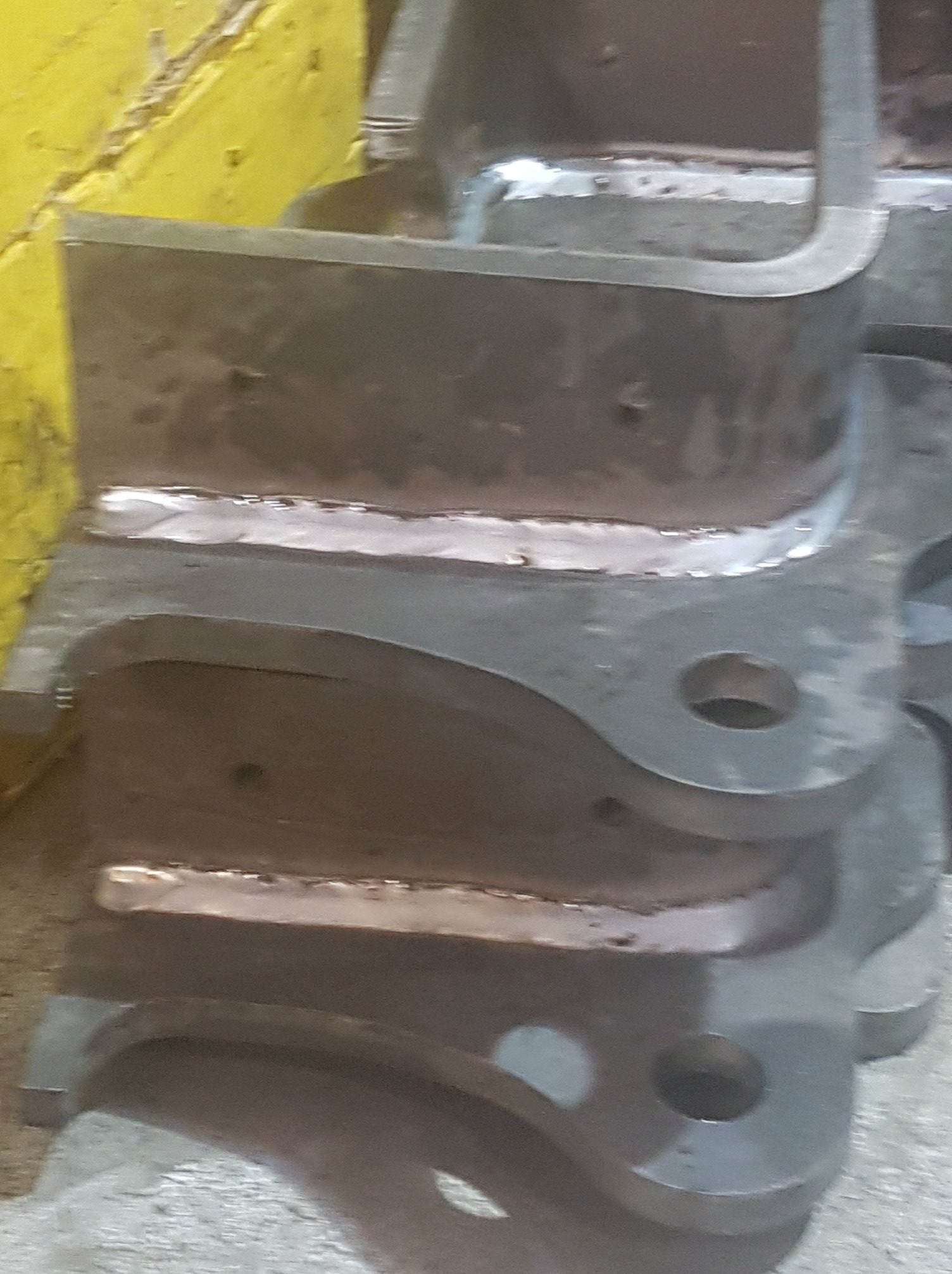 Stos metalowych elementów konstrukcyjnych połączonych spoiną, widoczne ślady obróbki i niedoskonałości spoin.