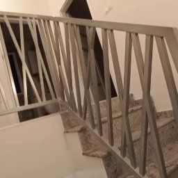 cayetann welding - Nowoczesna balustrada schodowa z metalowymi, krzyżującymi się elementami, zamontowana na marmurowych schodach w jasnym wnętrzu. Widok z dołu na górę.