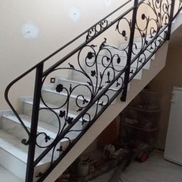 cayetann welding - Kuta balustrada schodowa z motywem roślinnym, czarna, zamontowana na marmurowych schodach. Elementy dekoracyjne w kształcie kwiatów i liści. Widok z dołu.