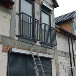 cayetann welding - Surowe balkony z czarnymi balustradami na tle budynku w trakcie budowy, z widoczną drabiną. Montaż rolet okiennych.