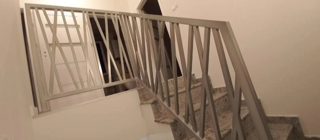 Nowoczesna balustrada schodowa z metalowymi, krzyżującymi się elementami, zamontowana na marmurowych schodach w jasnym wnętrzu. Widok z dołu na górę.