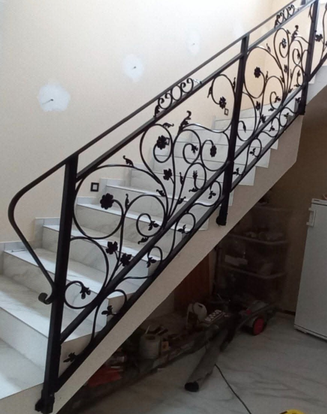 Kuta balustrada schodowa z motywem roślinnym, czarna, zamontowana na marmurowych schodach. Elementy dekoracyjne w kształcie kwiatów i liści. Widok z dołu.