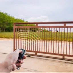 Otwieranie przesuwnej bramy wjazdowej za pomocą pilota; widoczne zielone fale radiowe.