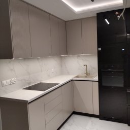 poli mebli - Nowoczesna kuchnia w beżowych odcieniach z białym blatem i marmurowym backsplash'em, wyposażona w czarny piekarnik i płytę indukcyjną.