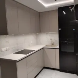 Nowoczesna kuchnia w beżowych odcieniach z białym blatem i marmurowym backsplash'em, wyposażona w czarny piekarnik i płytę indukcyjną.